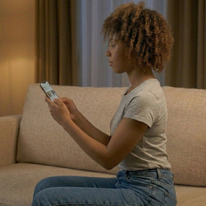 Woman sitting on a couch holding a smartphone in a dimly lit room.